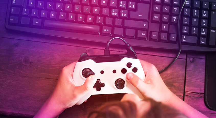 Eine weiße Spielkonsole wird vor einer schwarzen Tastatur auf einem Holztisch gehalten.