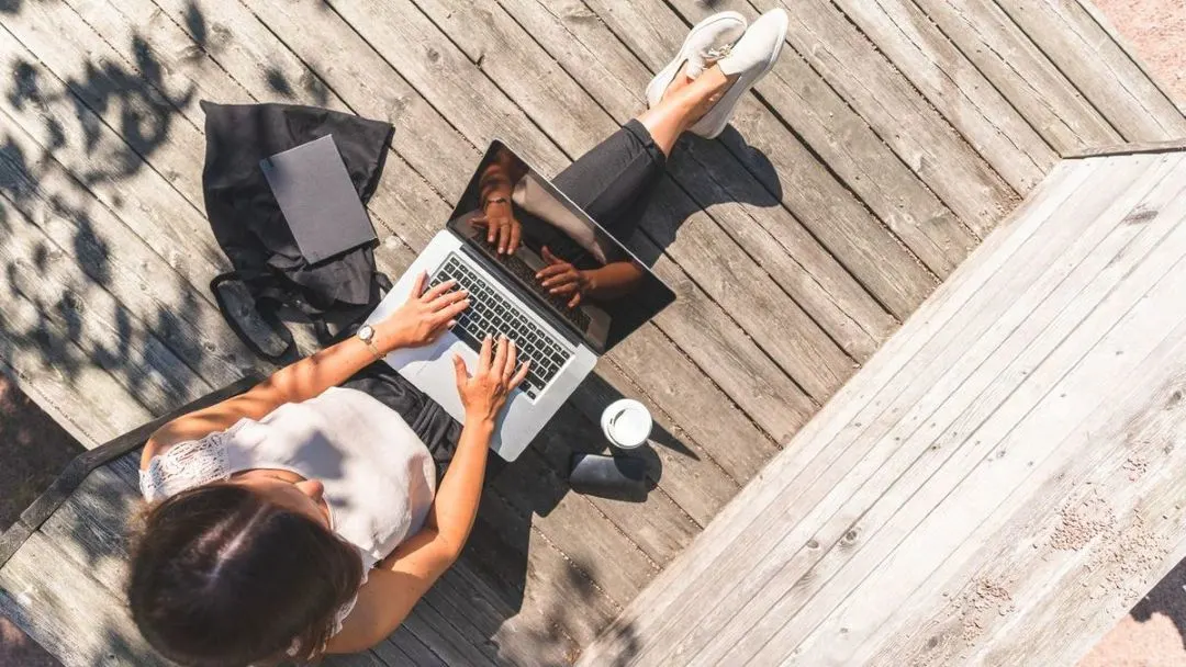 Frau arbeitet am Laptop auf Holzterrasse.