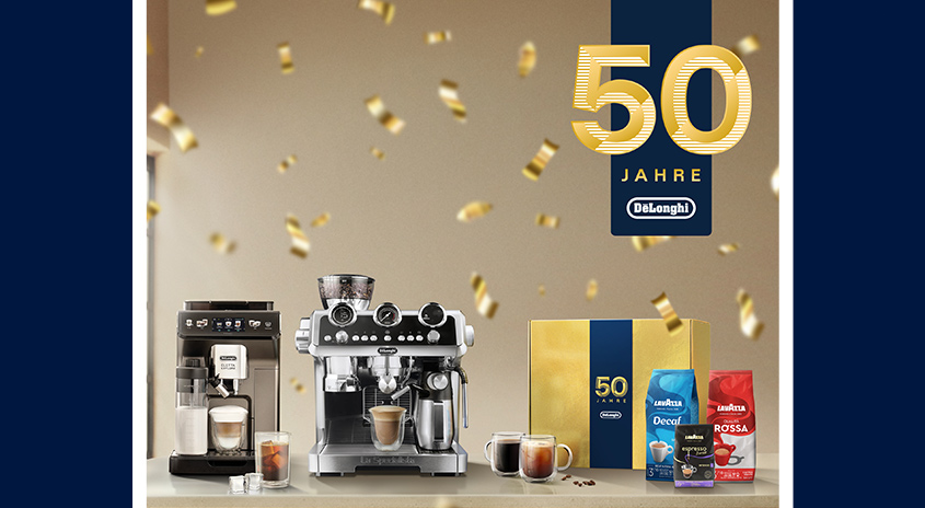 Zwei Kaffeemaschinen, Tassen, Kaffeepackungen und goldene Konfetti vor einem Banner "50 Jahre DeLonghi".