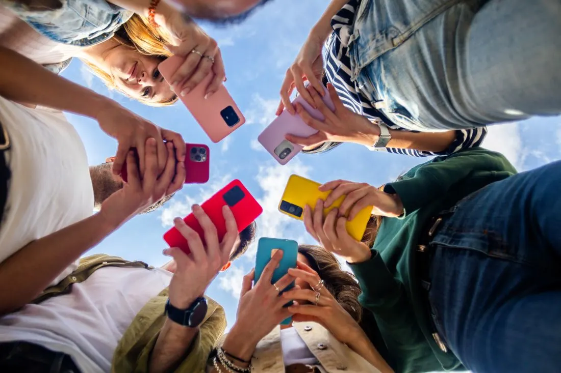 6 Personen stehen im Kreis und halten ihre bunten Smartphones in die Mitte, Foto von unten betrachtet