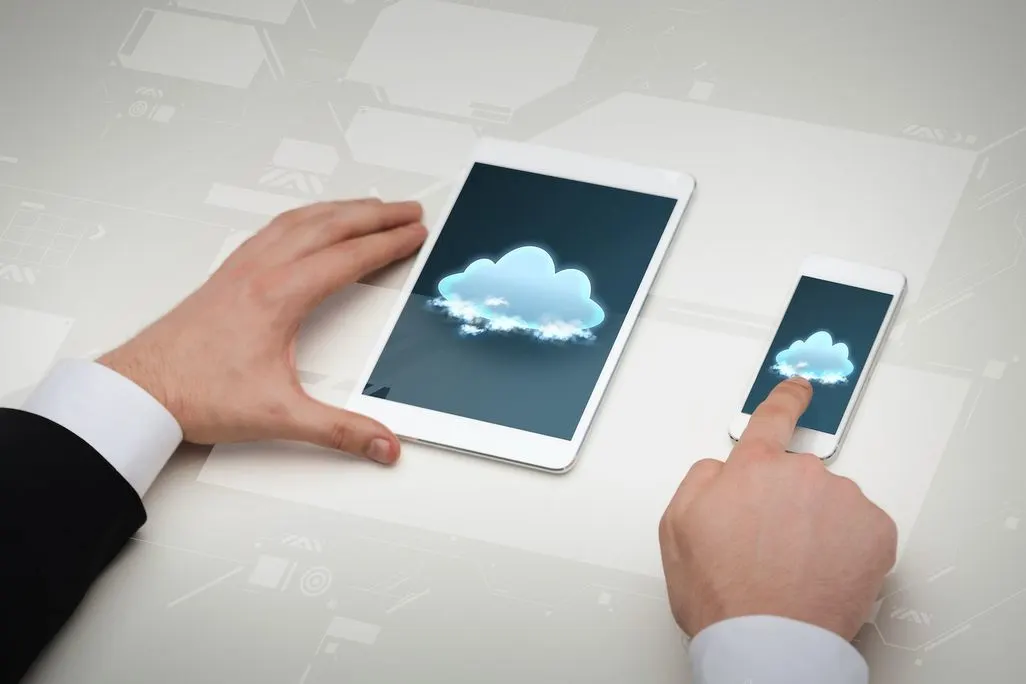 Zwei Hände bedienen Tablet und Smartphone mit einer Cloud Grafik auf dem Bildschirm.