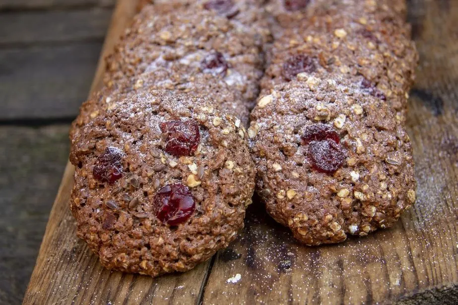 Schokoladige Haferkekse mit getrockneten Kirschen und Nussstücken auf Holzbrett.