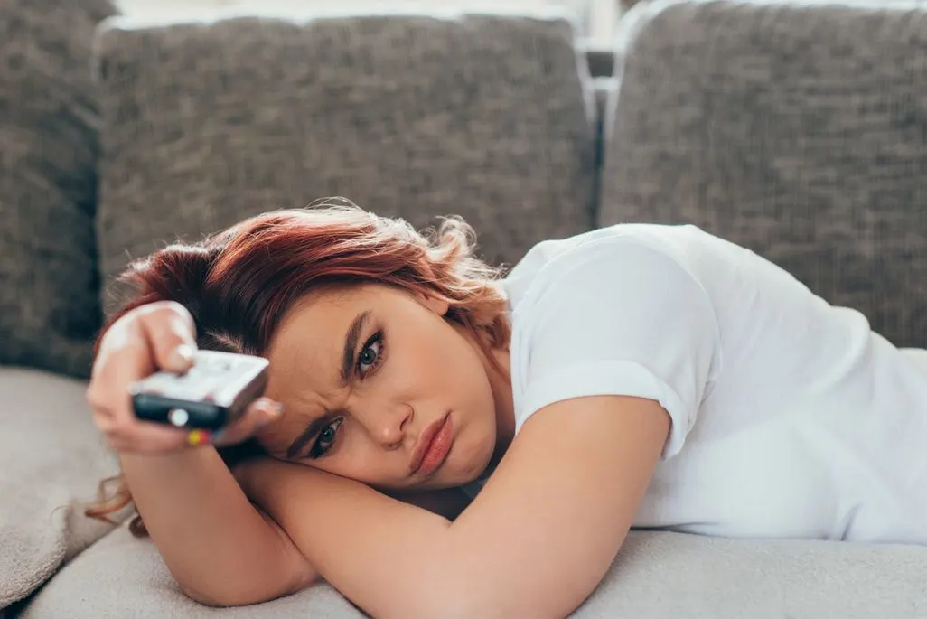 Eine Person liegt seitlich auf einem Sofa und hält eine Fernbedienung in der Hand