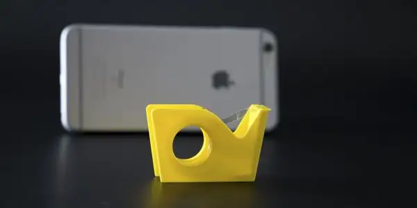 Gelber Klebebandroller steht vor einem silbernen Smartphone.