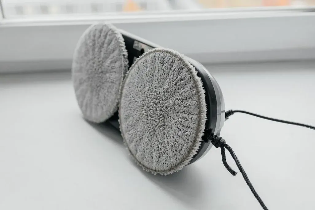 Ein Fensterputzroboter mit Reinigungspads an der Unterseite liegt auf einem Fensterbrett.