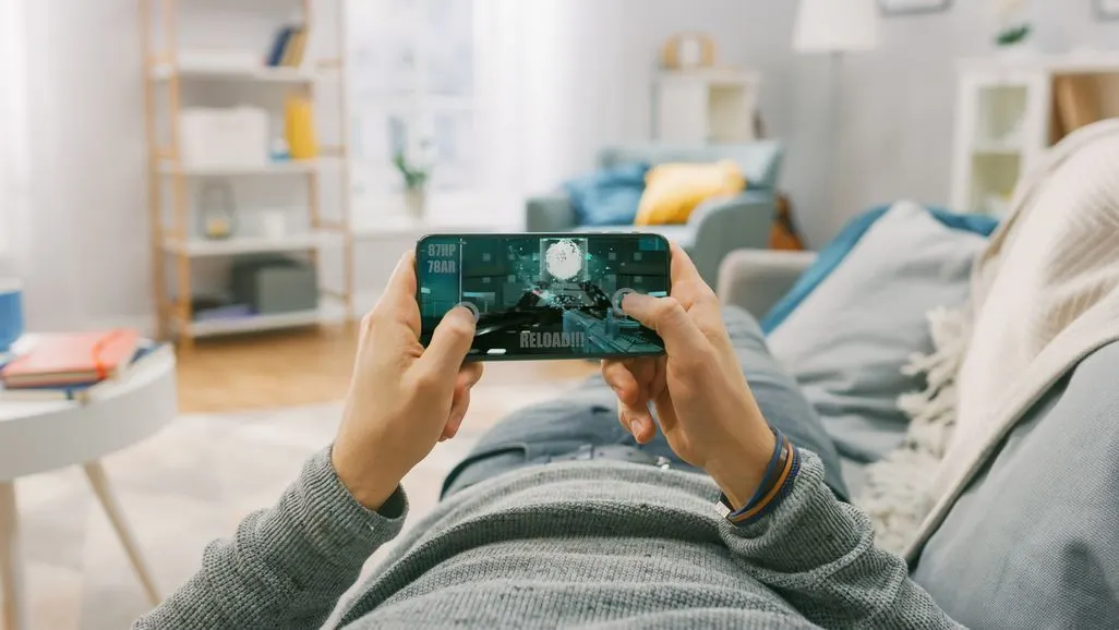 Person liegt auf Sofa und spielt Videospiel auf Smartphone