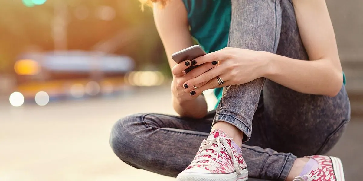 Eine Person sitzt draussen und benutzt ein Smartphone