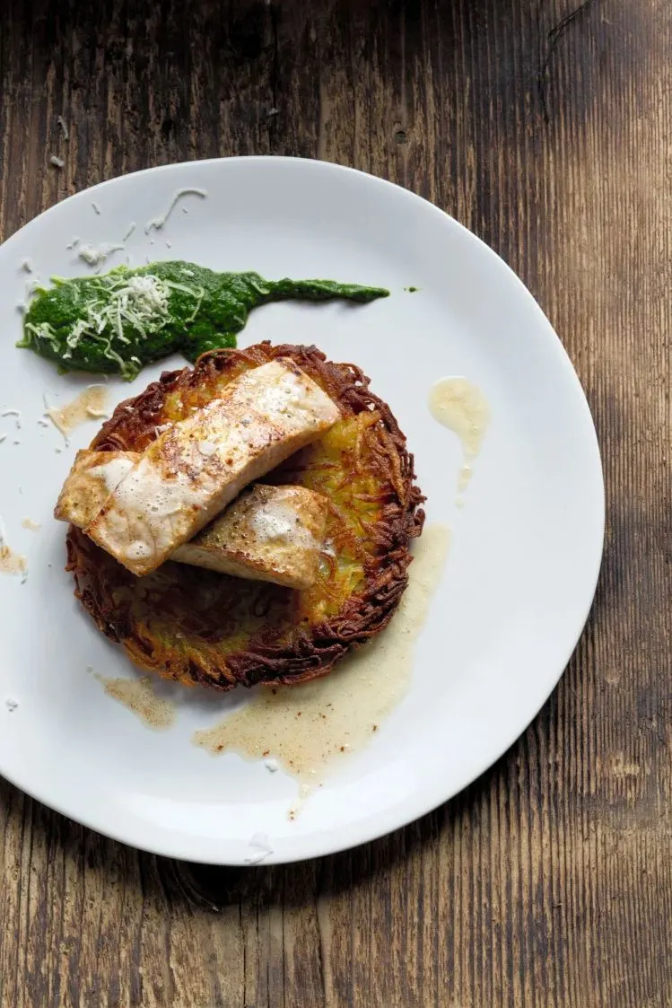 Wallerfiletschnitte auf Rösti garniert mit Spinat, angerichtet auf einem weißen Teller.