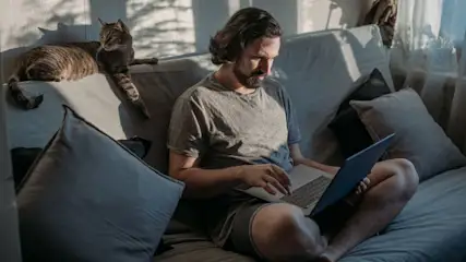Mann arbeitet entspannt mit Laptop auf Sofa im Homeoffice.
