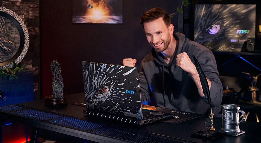 Ein MSI-Laptop mit einem Adlerbild steht auf einem dunklen Schreibtisch. Im Hintergrund sind Dekorationen und ein Bildschirm zu sehen.