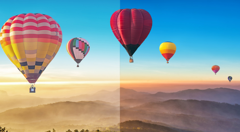 Mehrere bunte Heißluftballons schweben über hügeligen Landschaften unter einem blauen Himmel bei Sonnenaufgang.