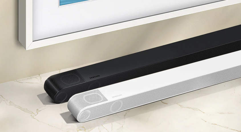 Zwei Soundbars, eine schwarz, eine weiß, liegen vor einer Wand. Über ihnen hängt ein gerahmtes Bild.