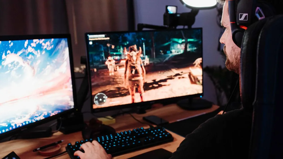 Ein Mann mit Headset sitzt an einem Schreibtisch und spielt an zwei Monitoren ein Computerspiel.