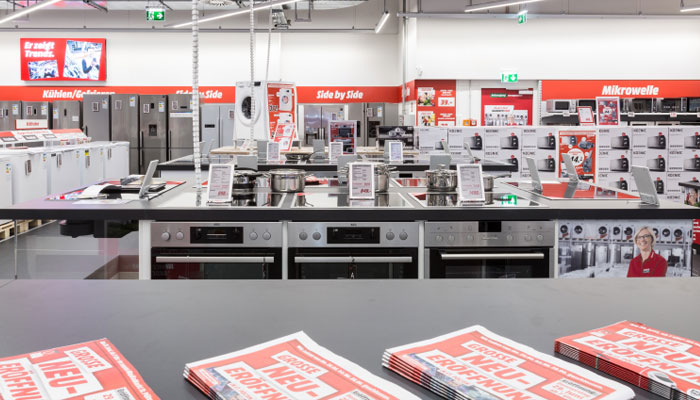 Ein Blick in ein Geschäft mit Haushaltsgeräten, darunter Öfen und Mikrowellen, mit roten Werbeschildern an den Wänden.