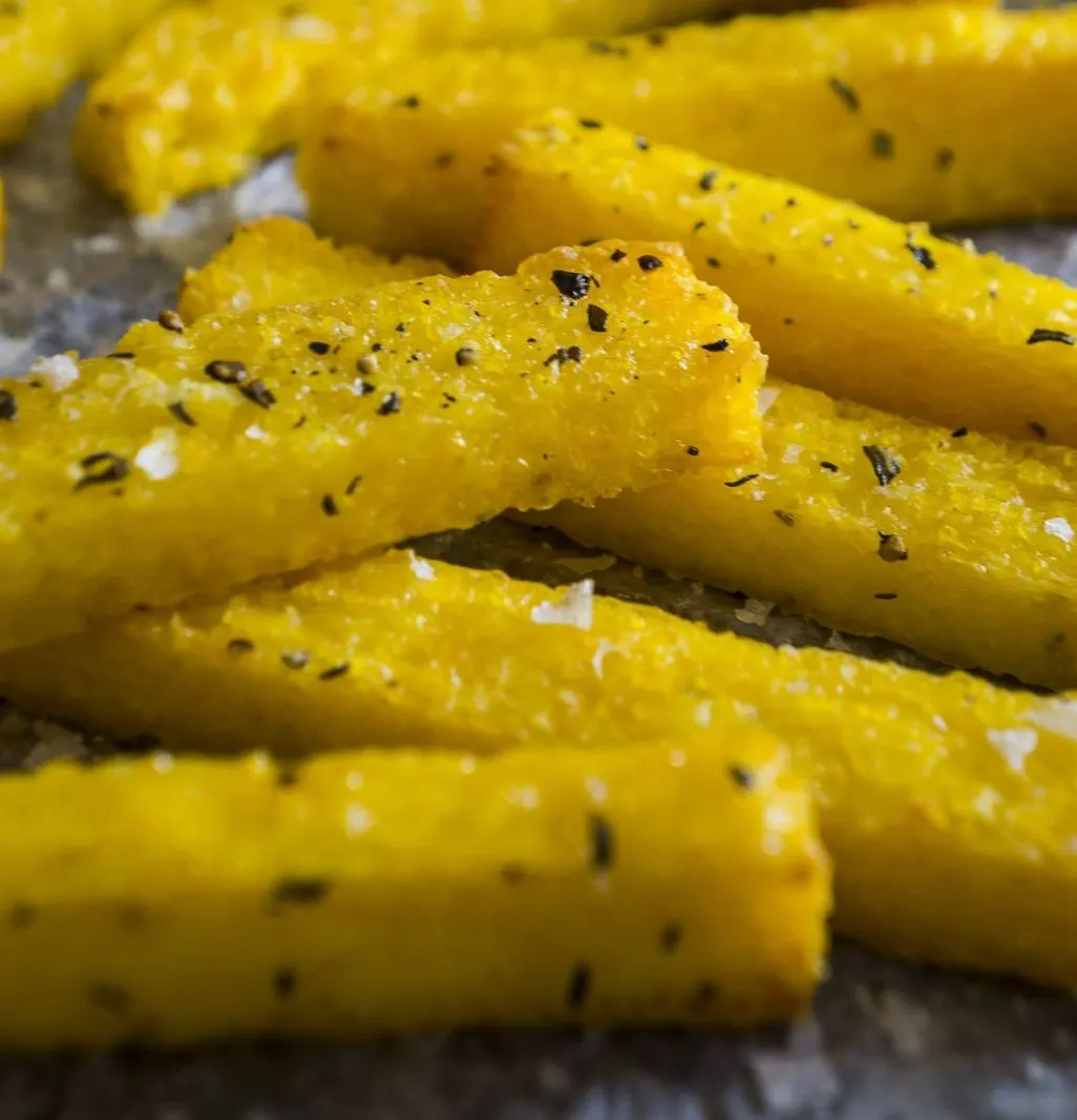 Knusprige Polentasticks mit Kräutern und grobem Salz auf Backpapier