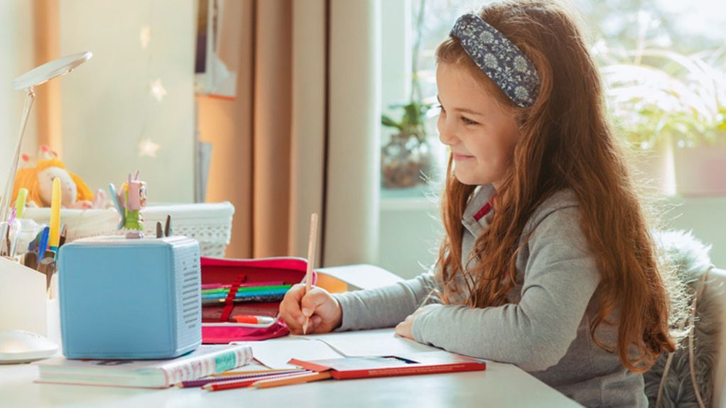 Mädchen sitzt an einem Schreibtisch und blickt lächelnd auf eine Toniebox.