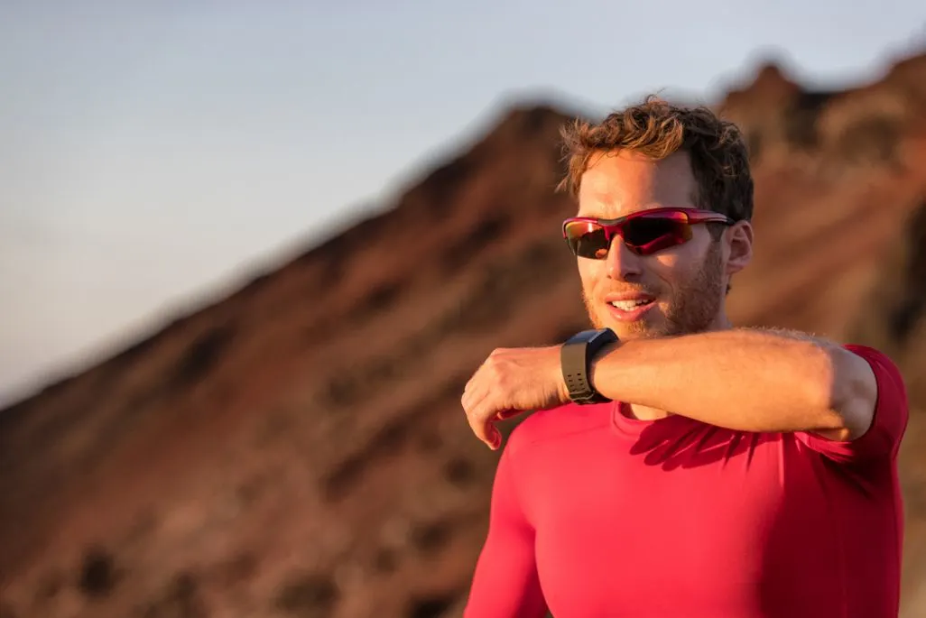 Mann in rotem Sportshirt trägt eine Smartwatch und steht vor einer bergigen Landschaft.