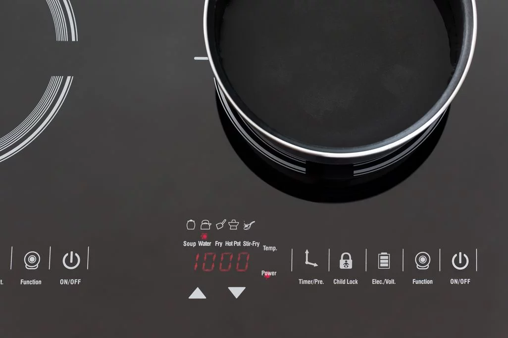 Blick von oben auf ein schwarzes Induktionskochfeld mit einem Topf, roter Digitalanzeige und weißen Bediensymbolen.