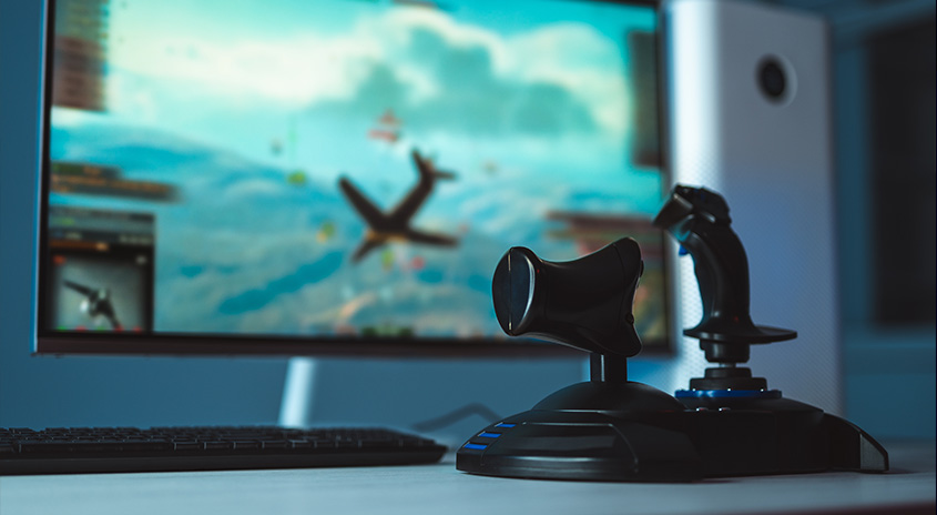 Ein Computerbildschirm zeigt ein Flugsimulationsspiel mit einem Joystick im Vordergrund auf einem Schreibtisch.