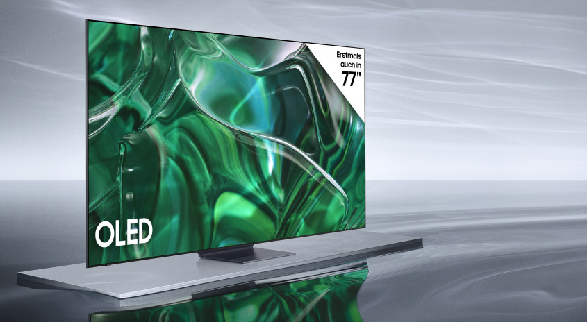 Ein OLED-Fernseher steht auf einem silbernen Sockel vor einem grauen Hintergrund. Der Bildschirm zeigt ein grünes, abstraktes Muster.