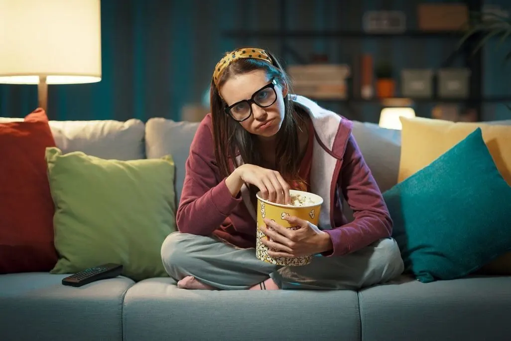 Eine Person sitzt im Schneidersitz auf einem Sofa und isst Popcorn