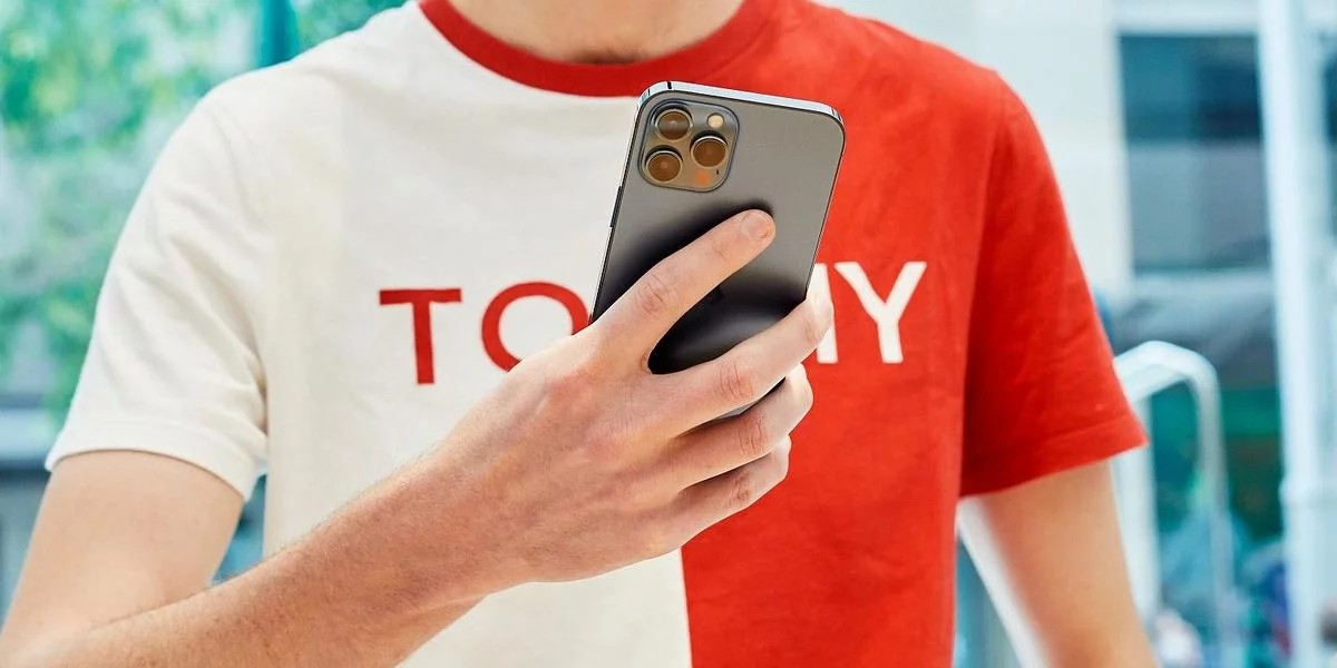 Ein Mann in einem weiß-roten T-Shirt hält ein iPhone in der Hand.
