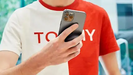 Ein Mann in einem weiß-roten T-Shirt hält ein iPhone in der Hand.