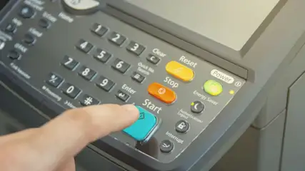 Finger drückt blaue Start-Taste auf Bedienfeld eines Multifunktionsgeräts mit Zahlentastatur.