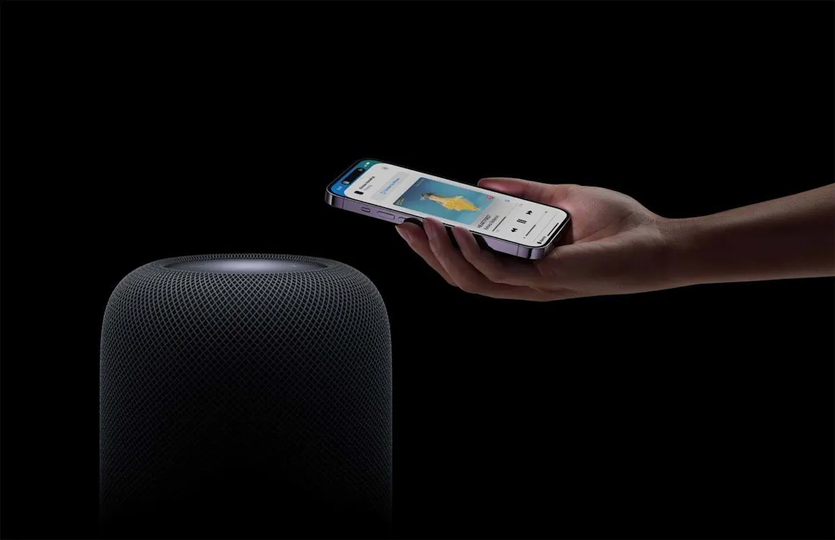 Eine Hand hält ein iPhone an einen HomePod vor schwarzem Hintergrund.