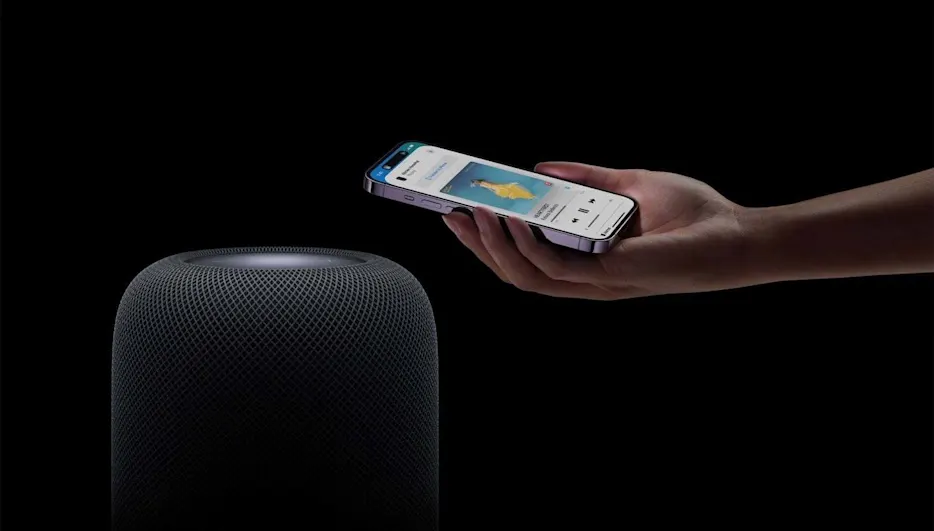 Eine Hand hält ein iPhone an einen HomePod vor schwarzem Hintergrund.