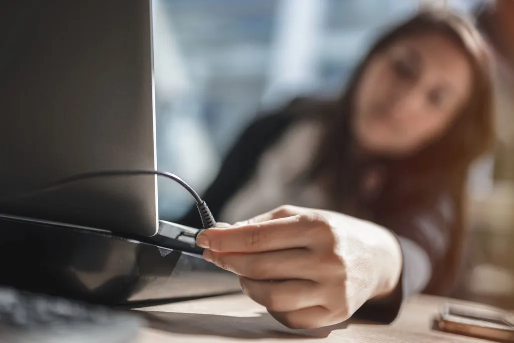 Hand steckt Ladekabel in Laptop-Anschluss am Arbeitsplatz