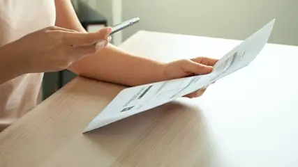 Person sitzt am Tisch und fotografiert ein Blatt Papier mit dem Smartphone.