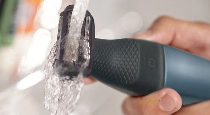 Eine Hand hält einen Rasierer unter fließendem Wasser, um den Scherkopf zu reinigen.