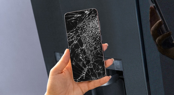 Hand hält ein Smartphone mit komplett gesplittertem Display vor einem dunklen Hintergrund.