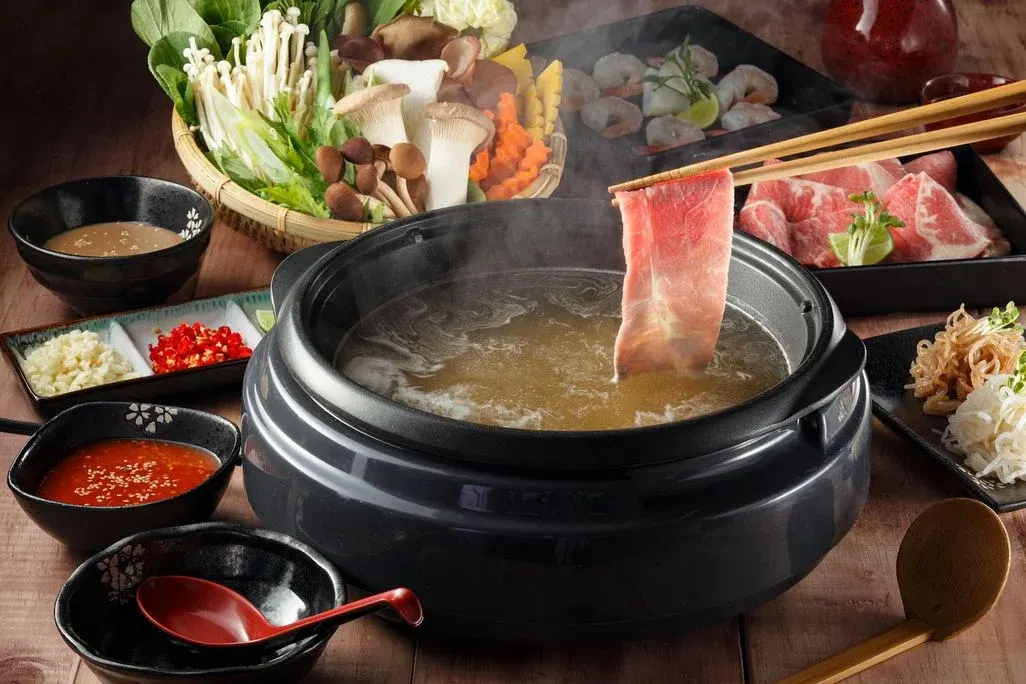 Schwarzer Pot mit Gemüse und Fleisch am Tisch.
