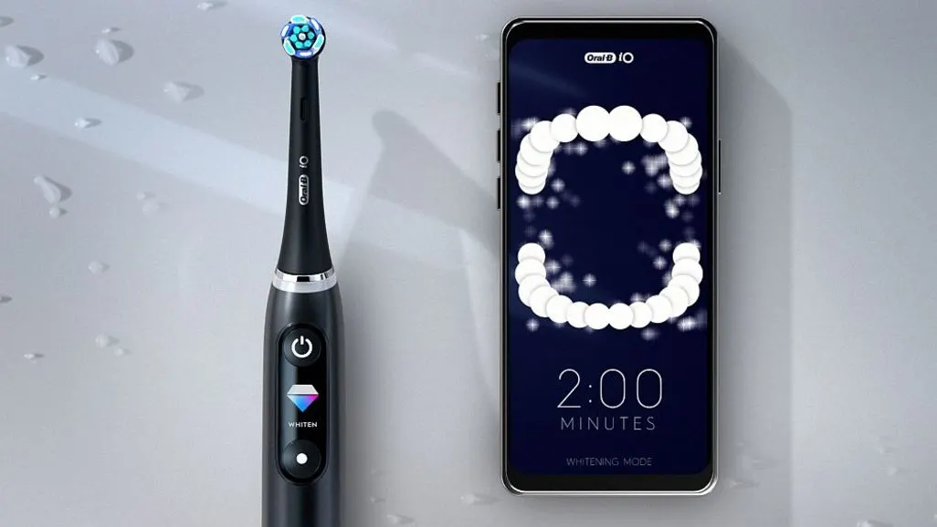 Schwarze elektrische Zahnbürste von Oral-B liegt neben Smartphone mit einer App, die ein Gebiss zeigt.