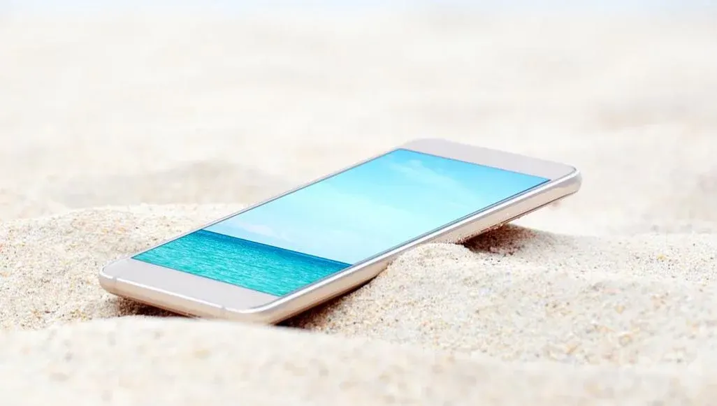 Ein Smartphone liegt im Sand und zeigt eine Aufnahme von Meer und Himmel.