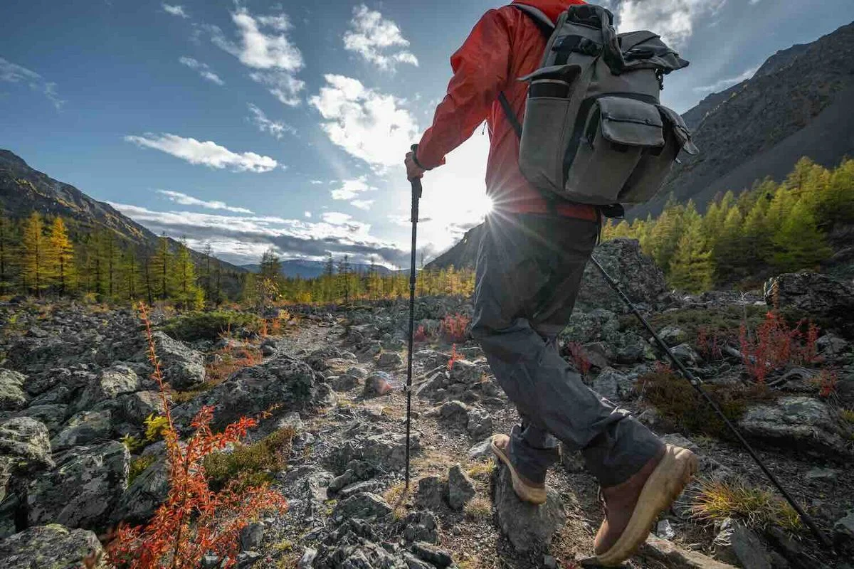 Wanderer mit roter Jacke und Rucksack wandert mit Wanderstöcken durch Gebirgslandschaft.