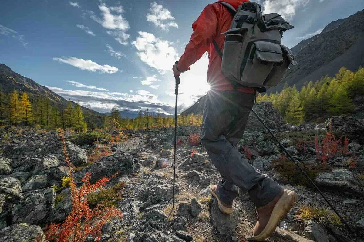 Wanderer mit roter Jacke und Rucksack wandert mit Wanderstöcken durch Gebirgslandschaft.