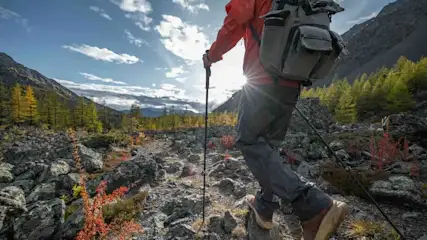 Wanderer mit roter Jacke und Rucksack wandert mit Wanderstöcken durch Gebirgslandschaft.