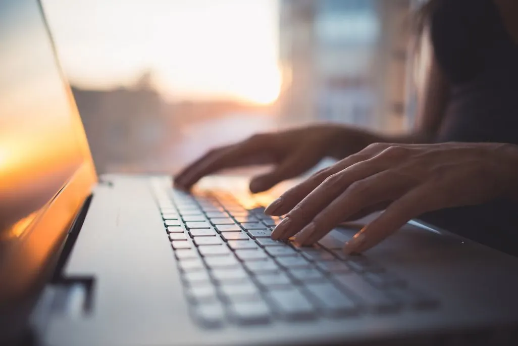 Nahaufnahme von Händen, die auf einer Laptop-Tastatur tippen, bei warmem Sonnenlicht.