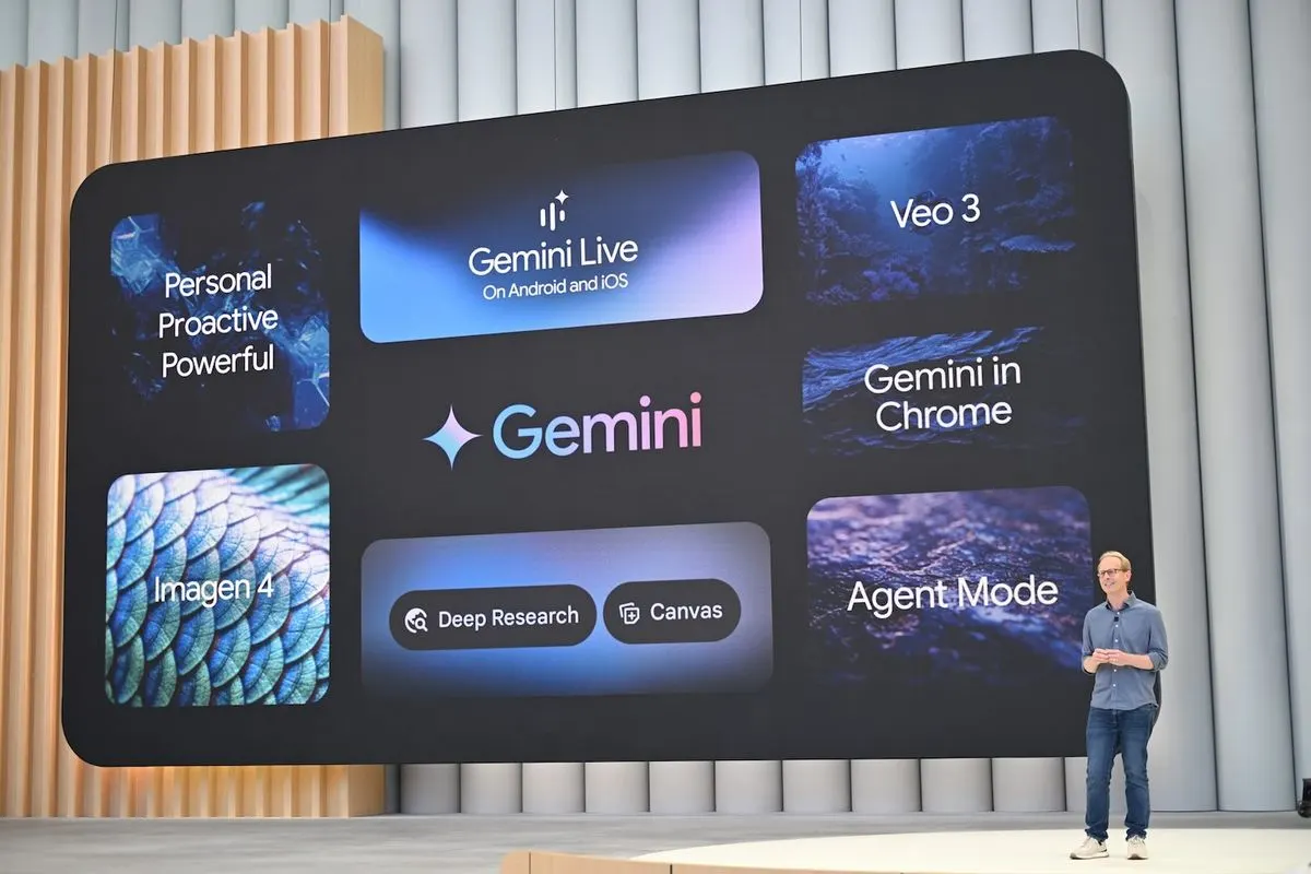 Eine Person steht auf einer Bühne vor einer großen digitalen Präsentationswand, auf der verschiedene Begriffe und Produkte rund um Googles AI "Gemini" angezeigt werden.