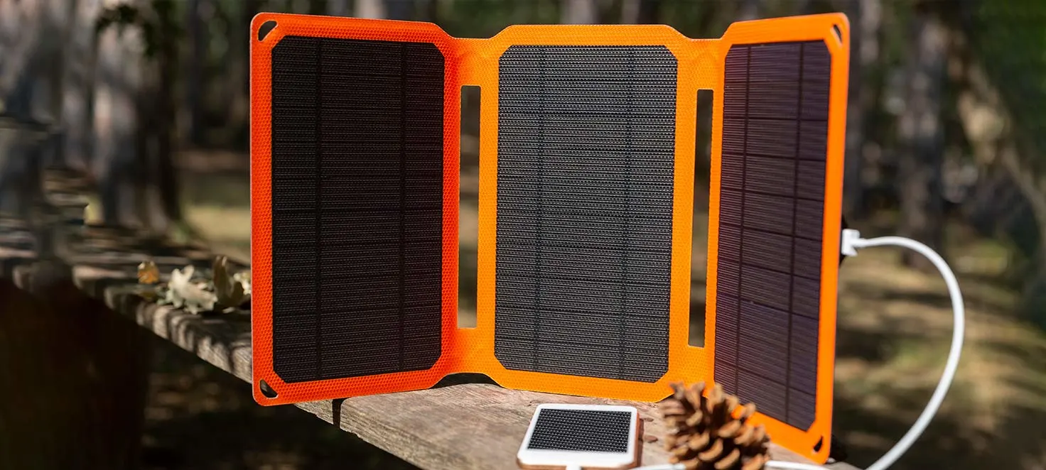 Ein orangefarbenes, dreiteiliges Solarpanel mit einem weißen Kabel und einem Smartphone auf einem Holztisch im Freien.