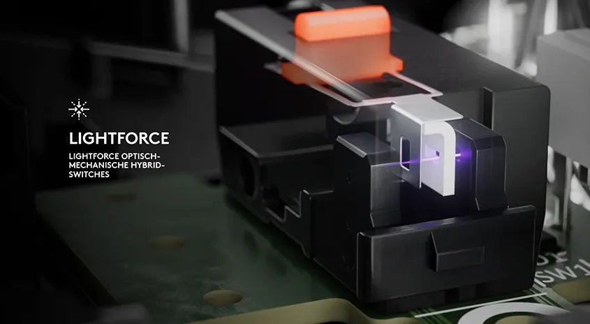 Nahaufnahme eines schwarzen, modularen optischen Schalters mit einem violetten Laserpunkt und einer orangefarbenen Taste auf einer grünen Leiterplatte.