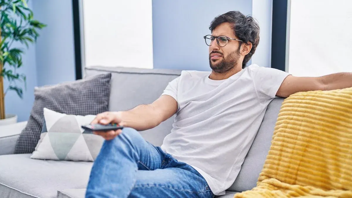 Eine Person sitzt entspannt auf einem Sofa und haelt eine Fernbedienung in der Hand
