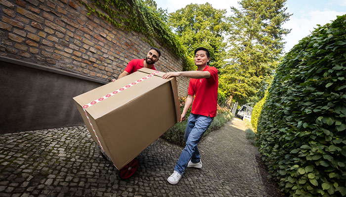 2 Männer mit MediaMarkt T Shirts liefern ein großes Haushaltsgerät in einem Karton.