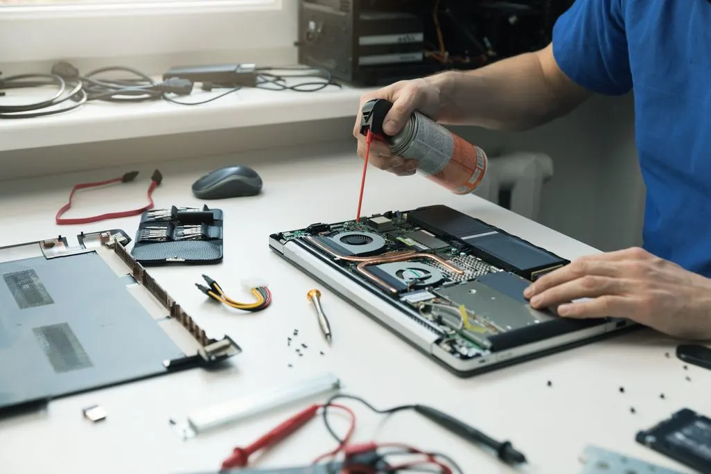 Techniker sprayt Druckluft in geöffneten Laptop zur Reinigung der Komponenten.