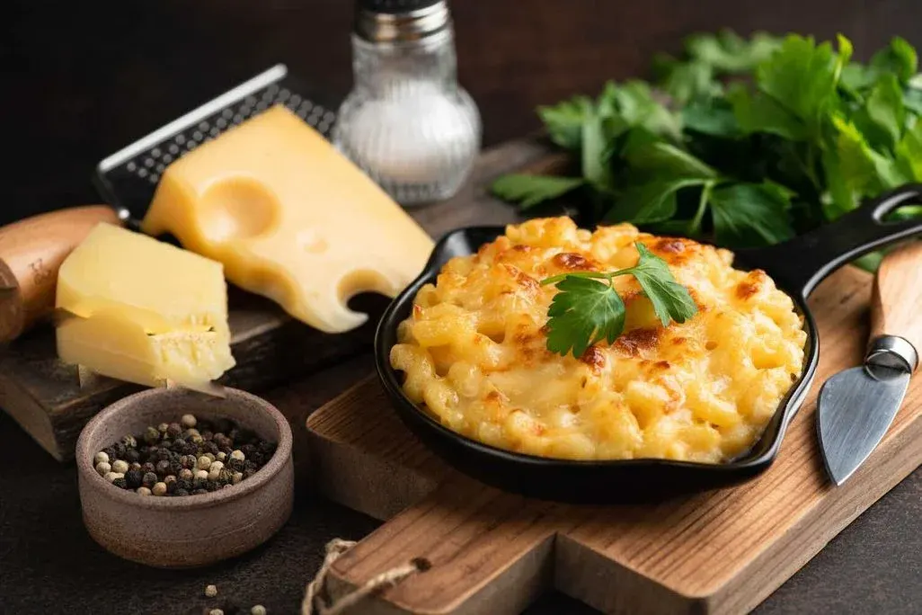 Kleines Pfännchen mit gebräuntem Mac 'n' Cheese und Käse im Hintergrund.