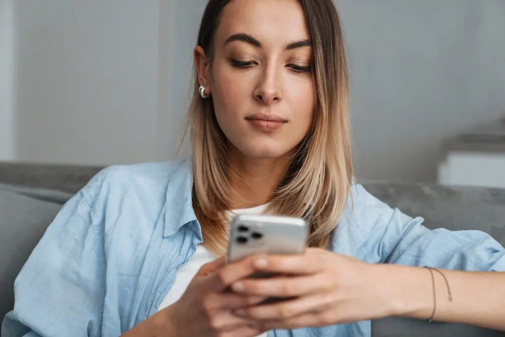Person sitzt auf Sofa und hält Smartphone in den Händen