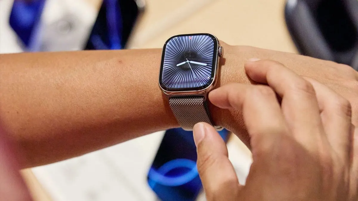 Person traegt eine moderne Smartwatch mit silbernem Armband am Handgelenk und bedient das Display mit dem Finger.
